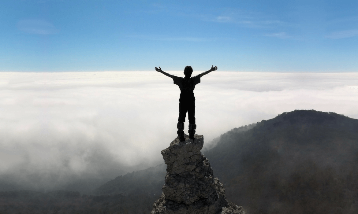 Person standing on the top of a rock stack on top of a mountain with outstretched arms